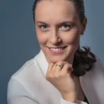 Profesjonalny portret biznesowy uśmiechniętej kobiety w białej bluzce na niebieskim tle.