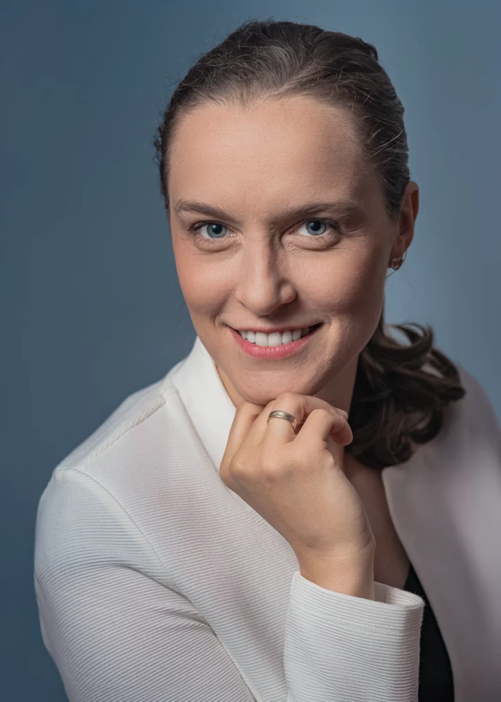 Profesjonalny portret biznesowy uśmiechniętej kobiety w białej bluzce na niebieskim tle.