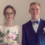 Młoda para w eleganckich strojach ślubnych uśmiecha się do kamery.