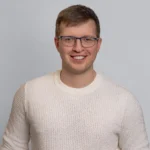 Mężczyzna w swetrze z uśmiechem pozujący do zdjęcia biznesowego.