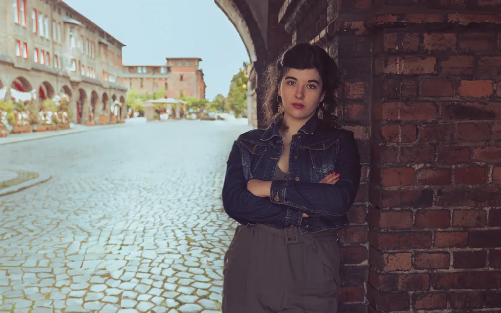 Kobieta w dżinsowej kurtce stojąca przed historycznym budynkiem z cegły.