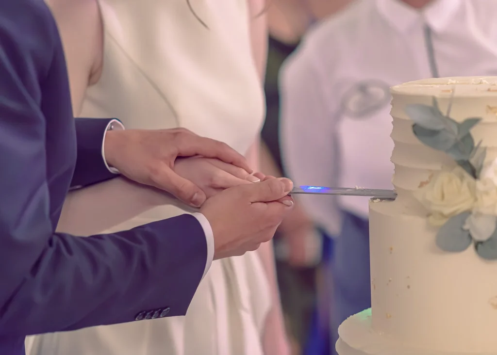 Para młoda kroi ślubny tort z białymi kwiatami na przyjęciu weselnym.