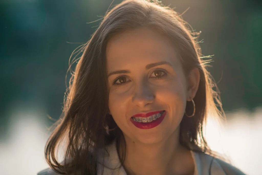 Uśmiechnięta kobieta z aparatem ortodontycznym na zębach podczas złotej godziny.