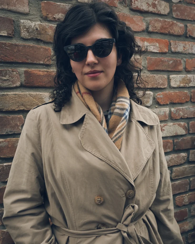 Kobieta w okularach przeciwsłonecznych i beżowym trenczu.