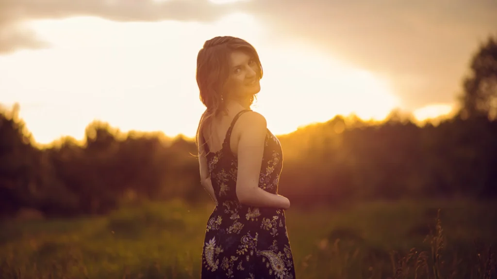 Uśmiechnięta kobieta ciesząca się delikatnym światłem złotej godziny.
